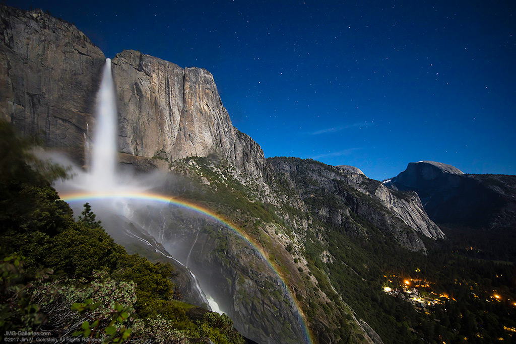 A wide arcing moonbow stretching across Upper Yosemite Falls on a clear night moonlit night in Yosemite National Park.